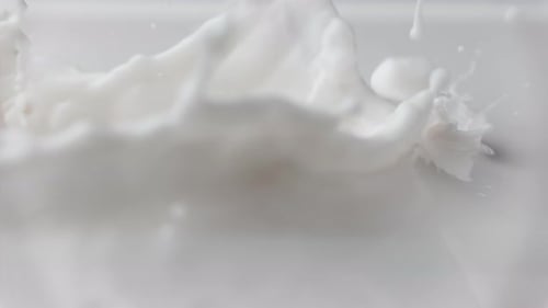 Goutte de lait frais tombant et éclaboussant dans un bassin laiteux déversant du lait au ralenti