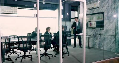 Multiracial business team attending strategy meeting in modern glass-walled office while male