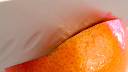 Very sharp knife cutting the surface of a tangerine. Close up macro shot. Clean cut.