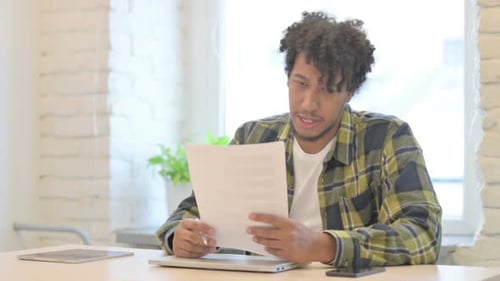 African Man Reading Documents in Office, Doing Paperwork