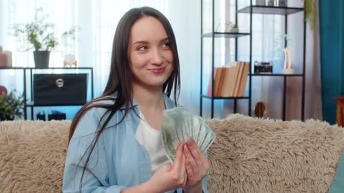 Smiling Woman Counts Dollar Bills on Living Room Couch