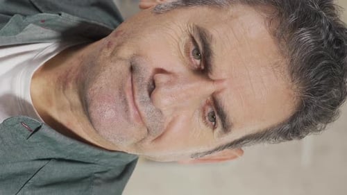 Vertical Video of Close-up shot of thoughtful mature adult man with gray hair sitting alone at home.