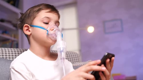 Boy With Nebulizer Using Cell Phone Indoors