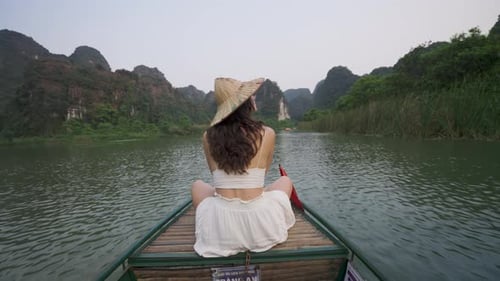 Woman in a straw hat sits on a boat in Vietnam, surrounded by stunning limestone cliffs