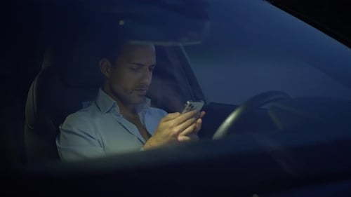 A Man is Using His Phone in a Car at Night Highlighting the Blend of Tech and Urban Life
