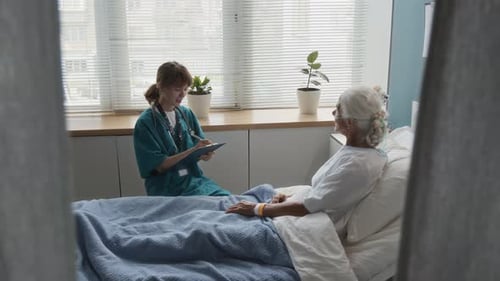 Medical Worker Asking Senior Woman Questions and Taking Notes in Hospital Room