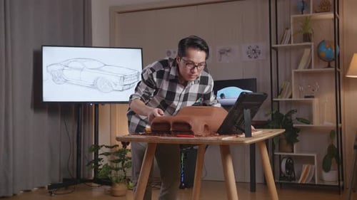 Asian Man Automotive Designer Looking At A Tablet And Using Rake Or Wire To Smooth Out The Surface