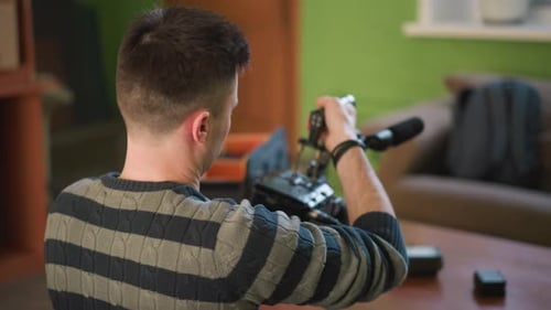 Man with Back to Camera Adjusting Video Equipment in Home Studio