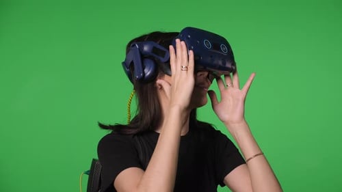 Portrait of a Young Woman Wearing Virtual Reality Glasses on a Green Background