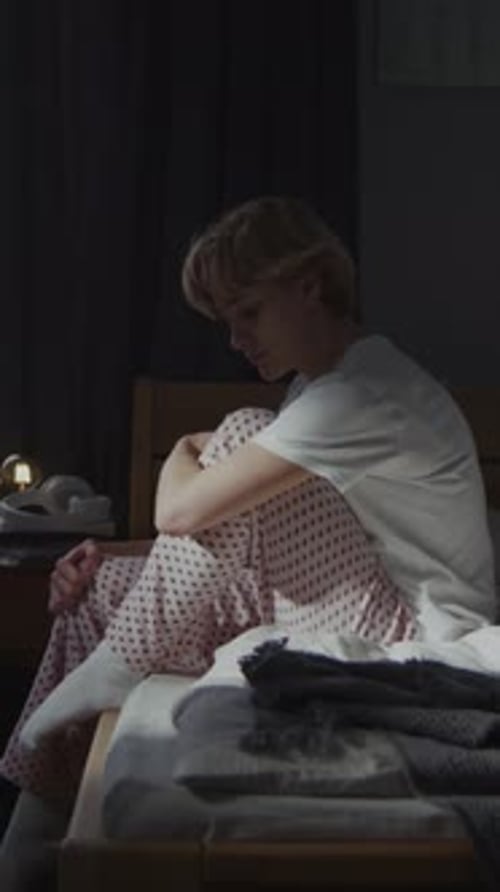 Individual Sitting on Bed in Dimly Lit Room