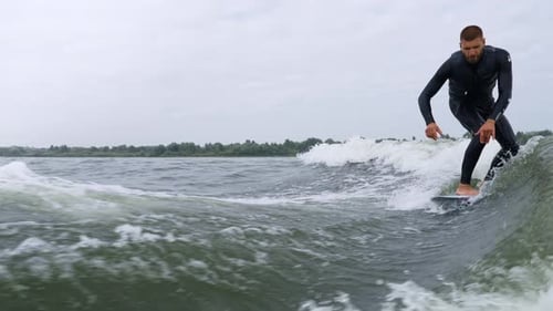 Man wake surfing on wavy lake in wetsuit