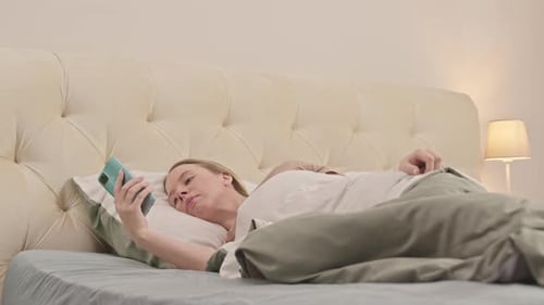 Woman Relaxes in Bed, Using Mobile Phone
