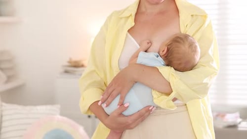 Woman Holding and Breastfeeding Baby Indoors Daytime