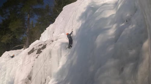 Wide angle view of a climber ascending a the summit of a wall of frozen ice