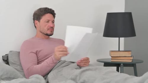 Man Reading Papers in Bed in the Morning