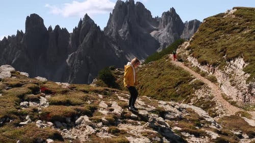 Woman in Yellow Jacket Goes Downhill Against Rocky Peak