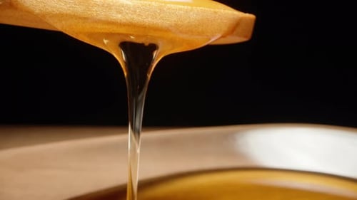 Honey from a wooden spoon flows into a plate, slider extreme close-up.
