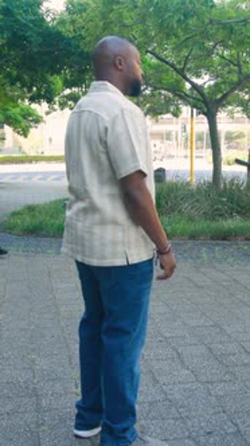 Man standing near tree on plaza shifting, inspecting offered phone for tech use returning to street