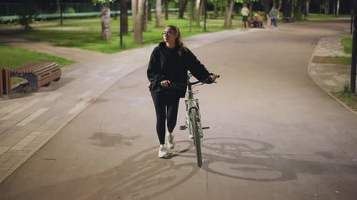 Woman Walking Confidently Through Serene Park Woman In Casual Attire Cycling Through Tranquil Park