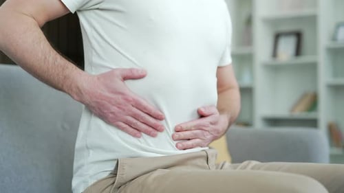 Close up. Male hands holding massaging stomach. Man in white T-shirt feels stomach pain on right