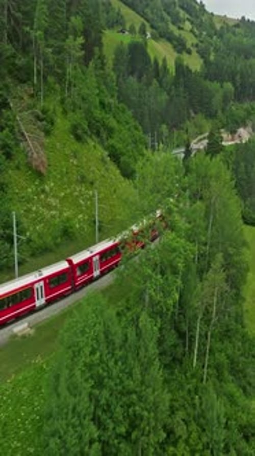 Luftaufnahme der malerischen Eisenbahnstrecke in der Schweiz im Sommer: Der rote Zug fährt durch eine wunderschöne Gegend