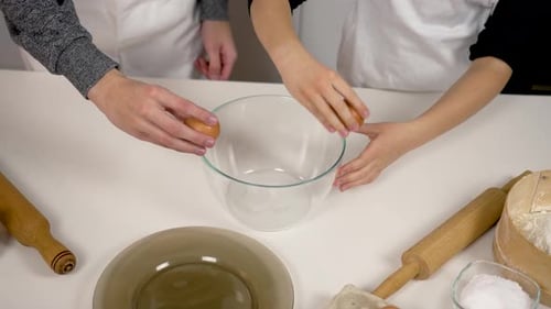 Hands of Children Boy and Girl Break Eggs on Glass Bowl and Release White and Yolk From Heel Close