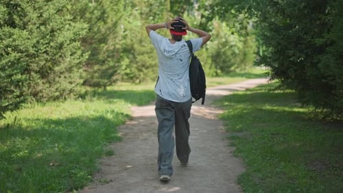 Individual Strolling Along Shaded Trail Man with Backpack Walking on Sunny Gravel Path Solitary Man