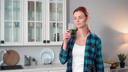 Portrait of a Charming Young Woman Holding a Glass of Fresh Green Smoothie in Her Hands Taking a Sip