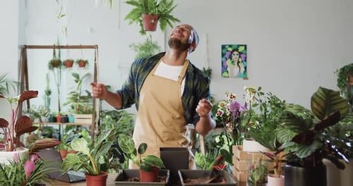Male florist gardener in apron dancing and working at flowers market. Attractive African American