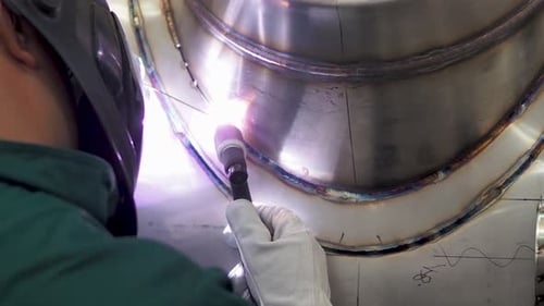 Skilled welder using TIG welding inside workshop, wearing mask. He is welding the stainless steel pa