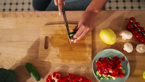 Mixed Race Woman Slicing Cucumber for Fresh Salad in Summer for Dinner Closeup Table with Vegetables