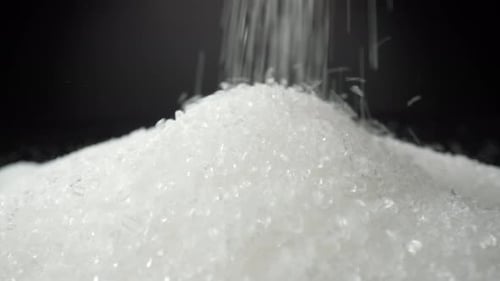 Weißer Zucker fällt zart auf einen glatten schwarzen Hintergrund