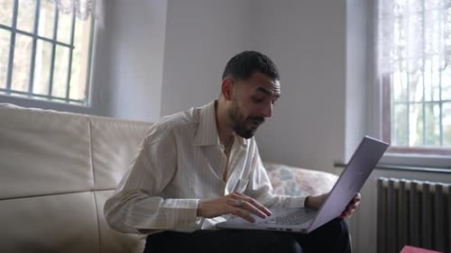 Man Using Laptop On Sofa in Bright Room
