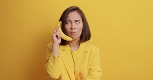 Confused woman holding banana like phone on yellow