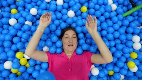 Woman Lying in Ball Pit Playing With Balls