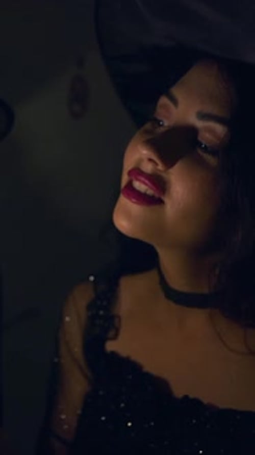 Dos mujeres colombianas con sombreros de bruja moviendo las manos alrededor de una bombilla encendida en un cuarto oscuro de Halloween
