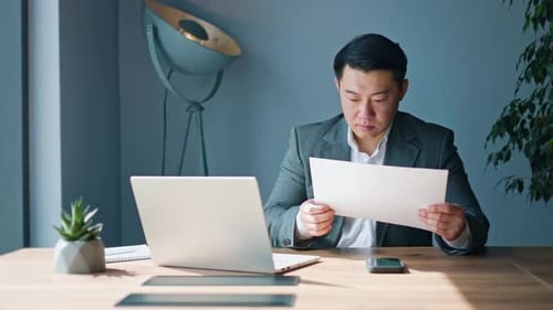 Attentive Asian Office Worker Rewriting Information From Document to Laptop