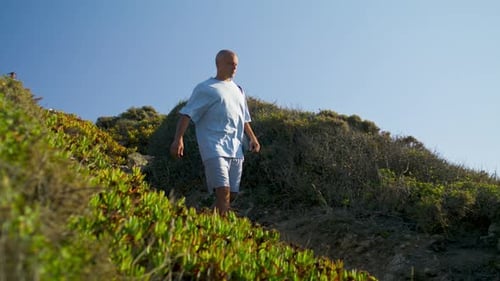 Man Walking Mountain Path Holding Yoga Mat in Sunlight. Athletic Guy Go