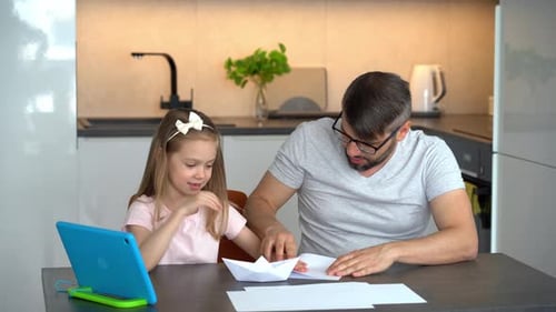 Padre e hija construyen botes de papel en origami y usan un tutorial sobre manualidades con tabletas