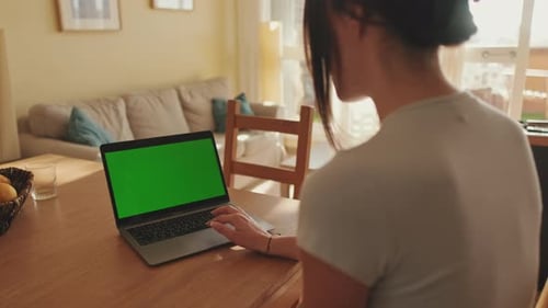 Young woman working on green screen chroma key laptop while sitting in apartment