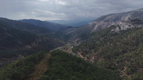 A wide aerial view of a mountainous landscape covered with dense green forest and rolling hills. A
