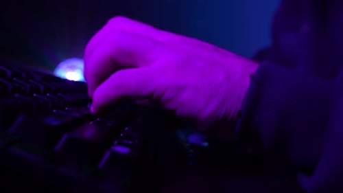 Unrecognizable Man Working on a Laptop Typing Fast on Keyboard in Neon Lighting