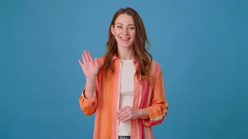 Smiling Woman Waves and Gestures on Blue Background