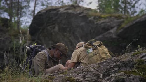 Black Father and Son with Backpacks Resting on Hill in Summer