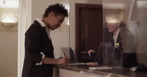Woman Signs Document at Hotel Reception Desk