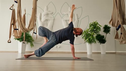 a male yogi with a beard does back stretching on the floor in a beautiful yoga studio to improve