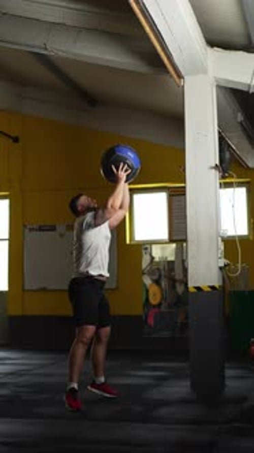 Hombre atlético haciendo ejercicio con pelota de pared con una pelota medicinal en un gimnasio durante el entrenamiento funcional