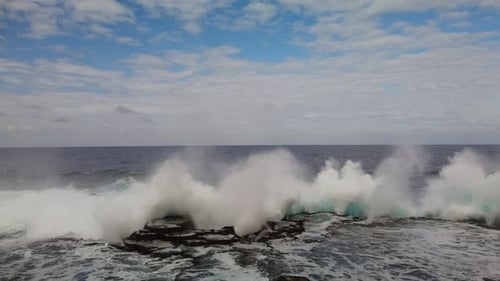 Aerial close up shot of sea waves are crashing into the rocky cliffs of a desert island before the