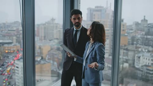 Business Partners Speaking Standing at Office Window Looking on City View