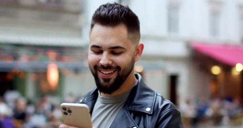 Close Up of Happy Young Handsome Smiling Male in Leather Jacket Texting Sms on Mobile Phone and